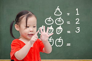 Asian child counting on hands in front of blackboard